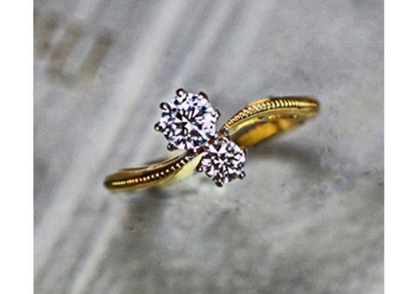 2つのダイヤモンドがウェーブしたゴールドリングに並ぶ婚約指輪
