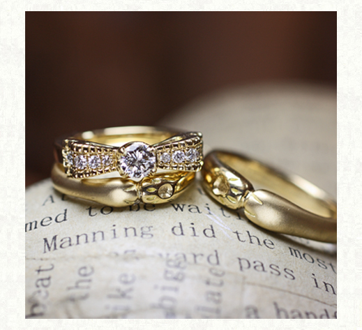 ネコの手のデザインのゴールド結婚指輪とリボンゴールドの婚約指輪を重ねてセットリングに