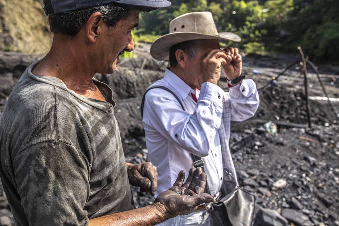 ルーペ片手に、エメラルドの鉱石を見て現金を渡している現地買い付け人